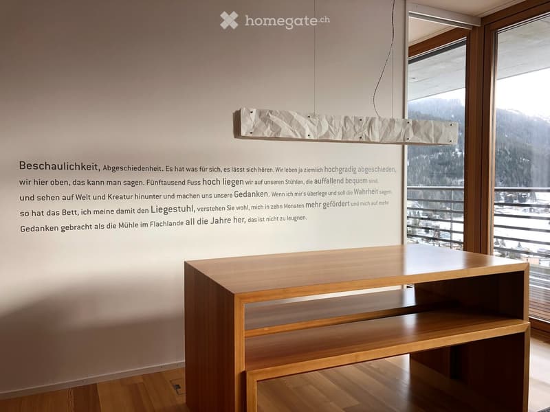 A modern, minimalist room with a wooden table, a pendant light, and large windows offering a scenic mountain view.