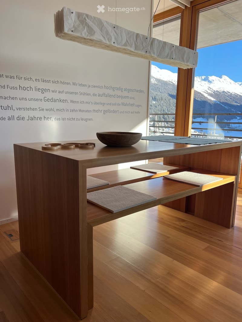 Modern room with wooden floor, large window showing mountain view, wooden table with a bowl, and a hanging lamp.