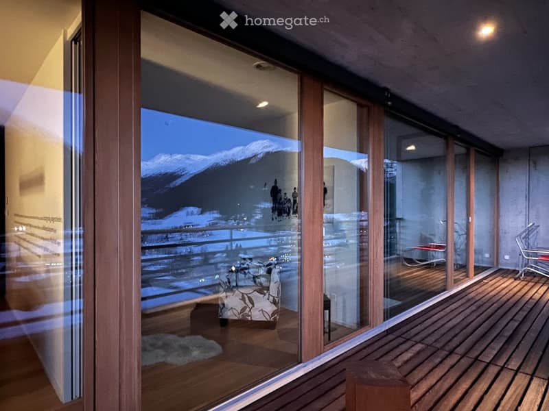 Balcony with wooden decking, large glass windows, and a view of snow-capped mountains.