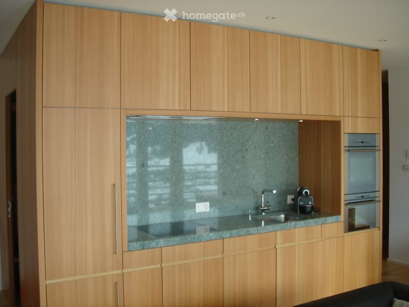 Modern kitchen with light wooden cabinets, granite countertop, sink, faucet, oven, and coffee maker.