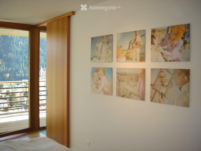 Bedroom with a large window offering a scenic mountain view, a bed, and several framed photographs on the wall.