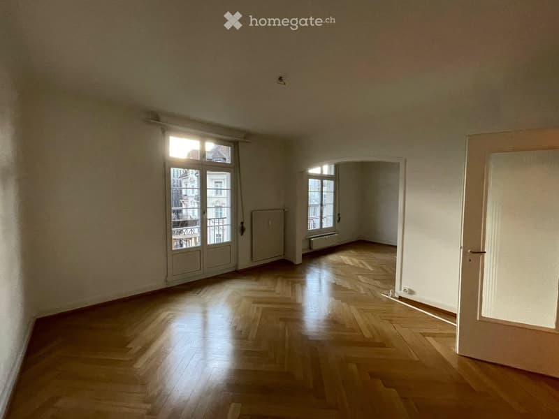 Empty room with wooden flooring, large windows, and a door leading to another space.