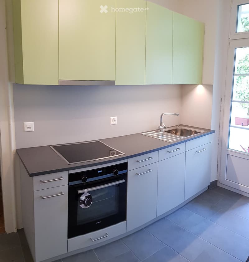 Modern kitchen with light-colored cabinets, stainless steel sink, induction cooktop, and built-in oven.