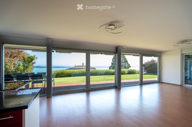 Bright, open-plan room with wooden flooring, large sliding glass doors leading to a patio, and a dining area with a table and chairs.
