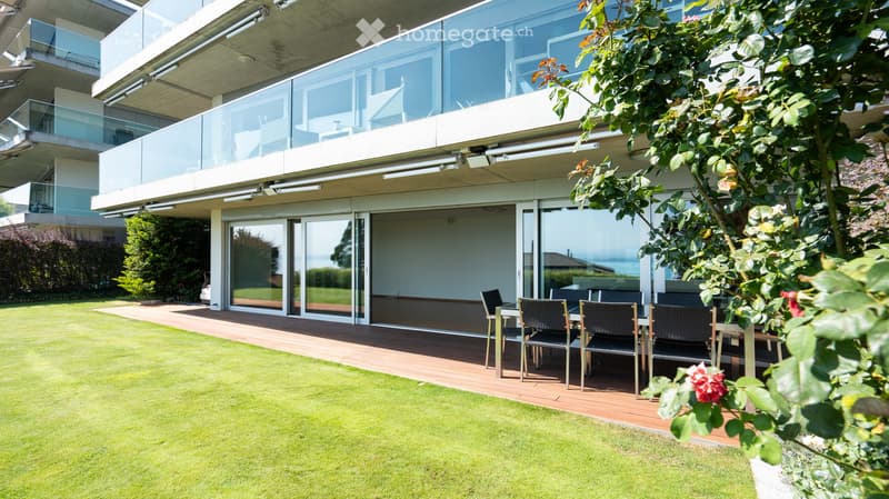 Well-maintained garden with a wooden deck, outdoor dining set, and modern house with large glass windows and balconies.