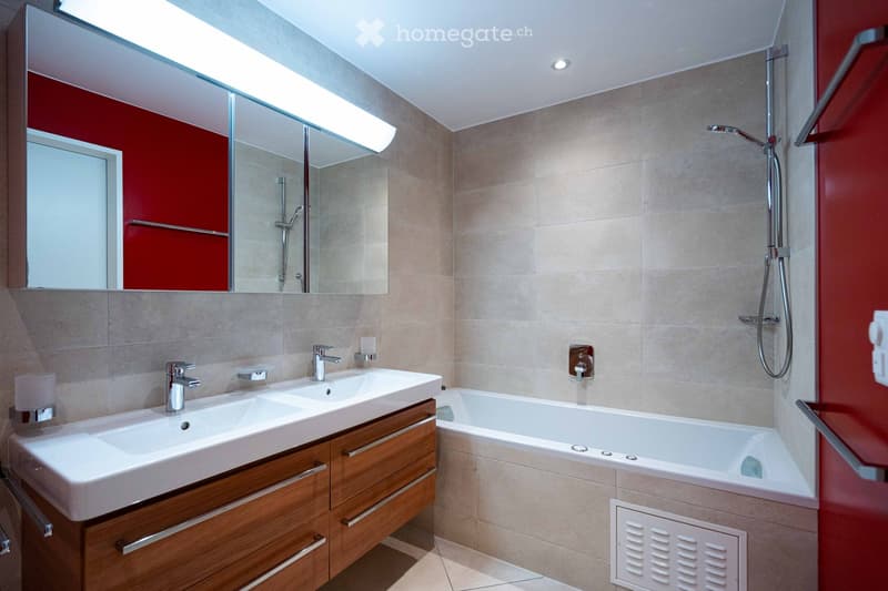 Modern bathroom with double sink, wooden cabinet, bathtub, large mirror, and shower fixture.
