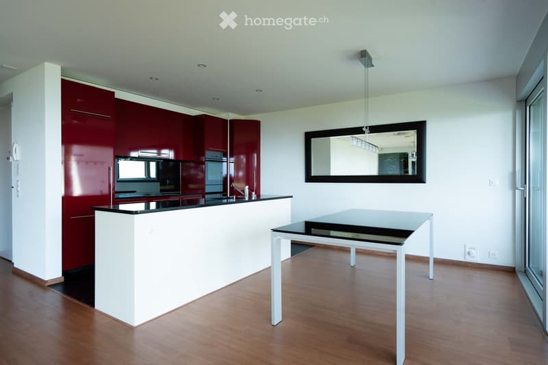 Modern kitchen with red cabinets, white counter, black countertop, glass table, and a mirror on the wall.