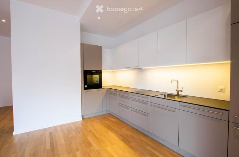 Modern kitchen with white cabinets, wooden flooring, and built-in appliances including an oven and sink.