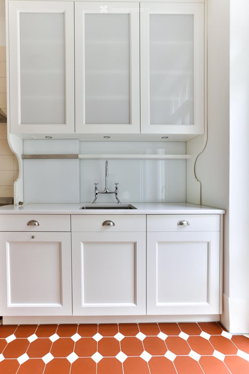 White kitchen with modern cabinets, a stainless steel sink, and a sleek faucet. The floor features a distinctive orange hexagonal tile pattern.