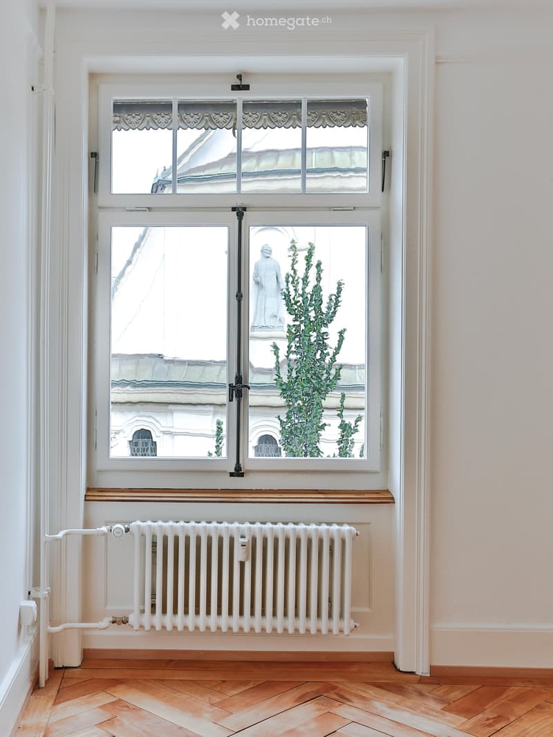 Empty room with wooden floor, white radiator, and large window with decorative glass panels and shutters.