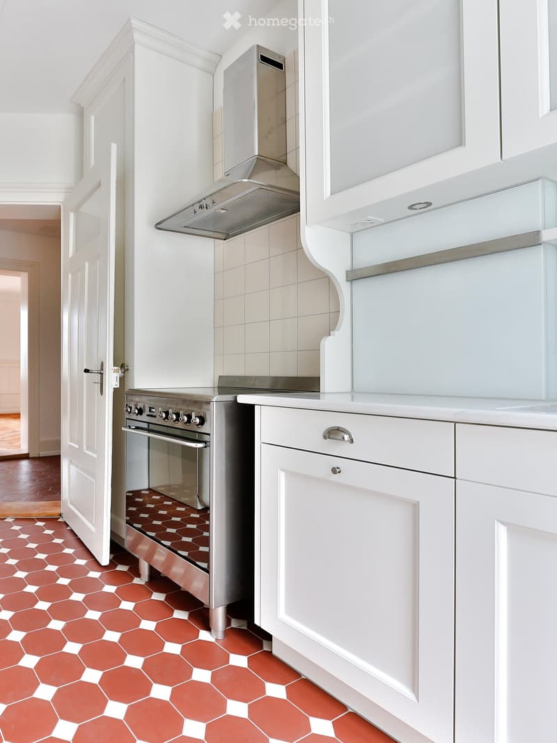 Modern kitchen with white cabinets, stainless steel oven, range hood, and hexagonal terracotta tiles on the floor.