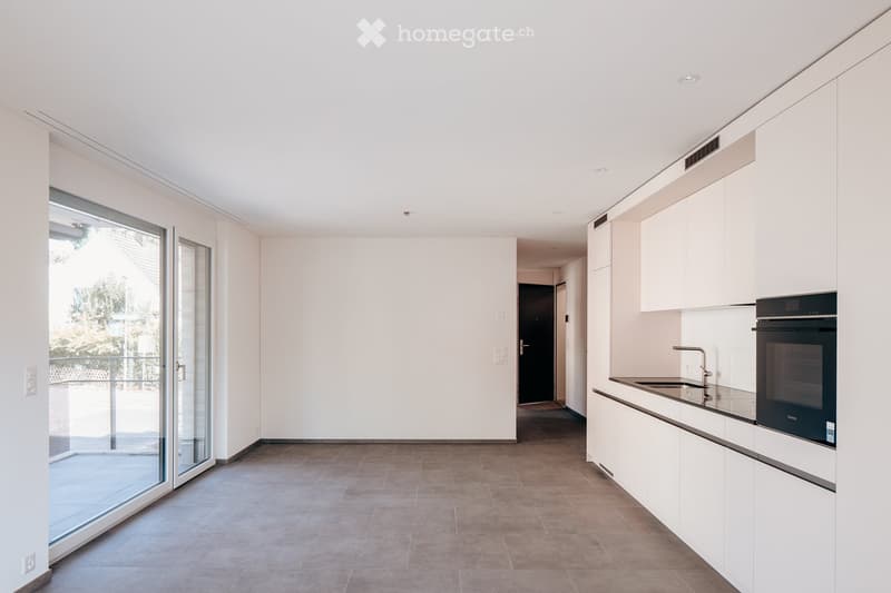 Modern kitchen with white cabinets, a sink, a faucet, and an oven. The space features large glass doors leading to a balcony.