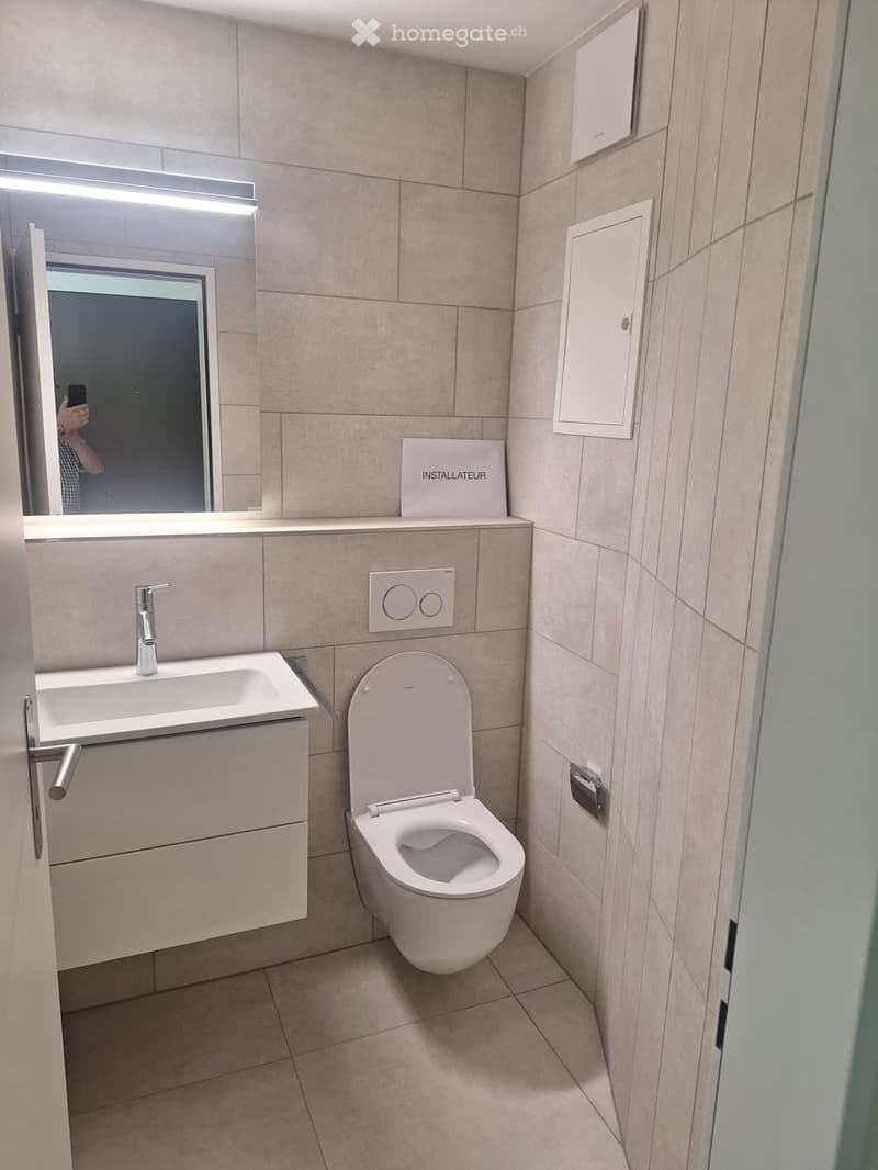 Modern bathroom with beige tiles, a toilet, a sink with a modern faucet, a mirror, and a cabinet.