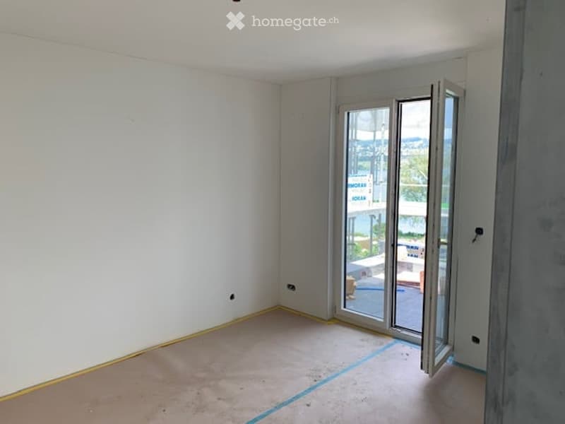 Empty room with white walls, wooden floor, and large sliding glass door leading to a balcony.
