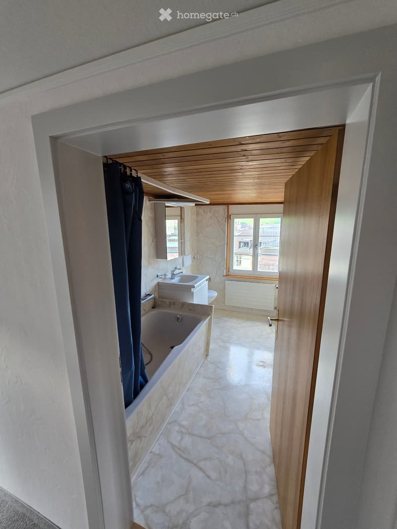 Bathroom with a bathtub, sink, toilet, and mirror. The room features a stone-tiled floor and a wooden ceiling.