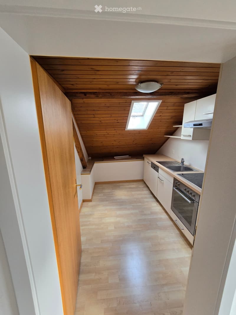 Empty kitchen with light wooden flooring, white cabinets, and a skylight window above the sink area.