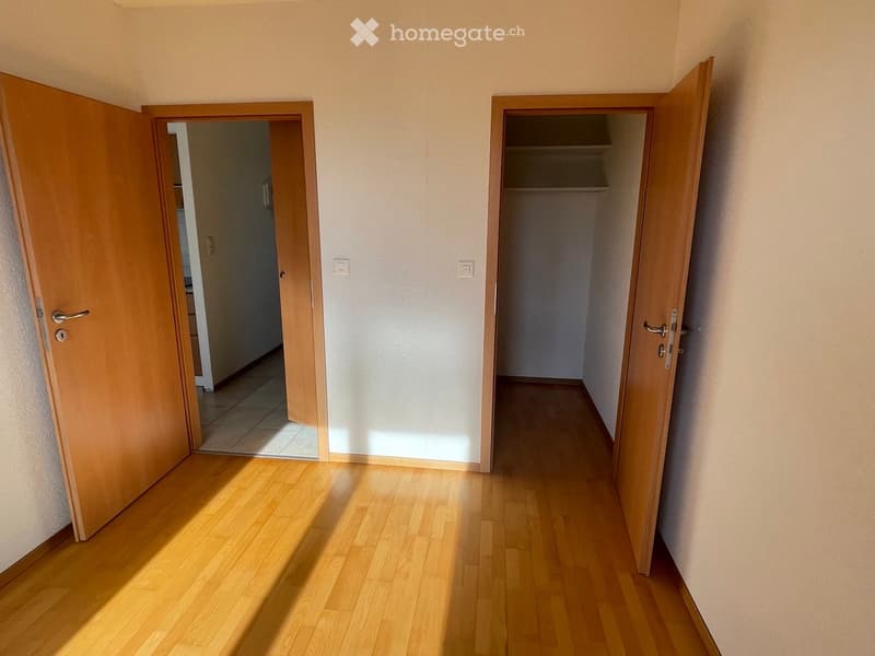 Empty hallway with wooden flooring, two open doors leading to other rooms, and light-colored walls.