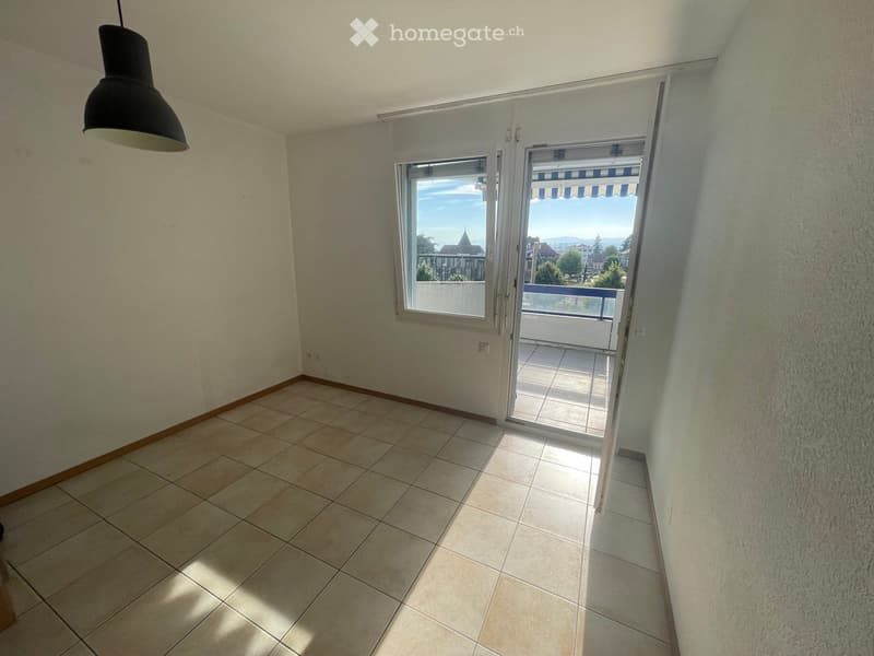 Empty room with tiled floor, white walls, large window, and sliding glass door leading to a balcony.