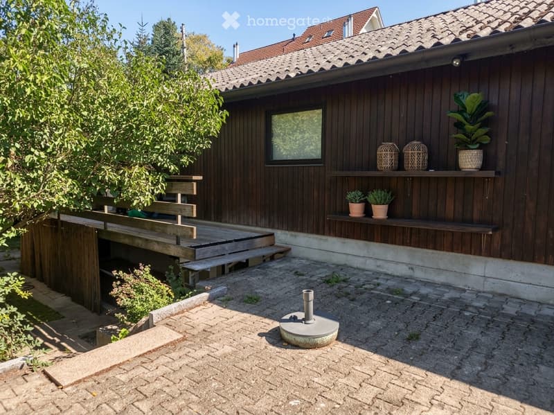 Wooden house with a raised wooden deck, small garden area, and decorative items on shelves.