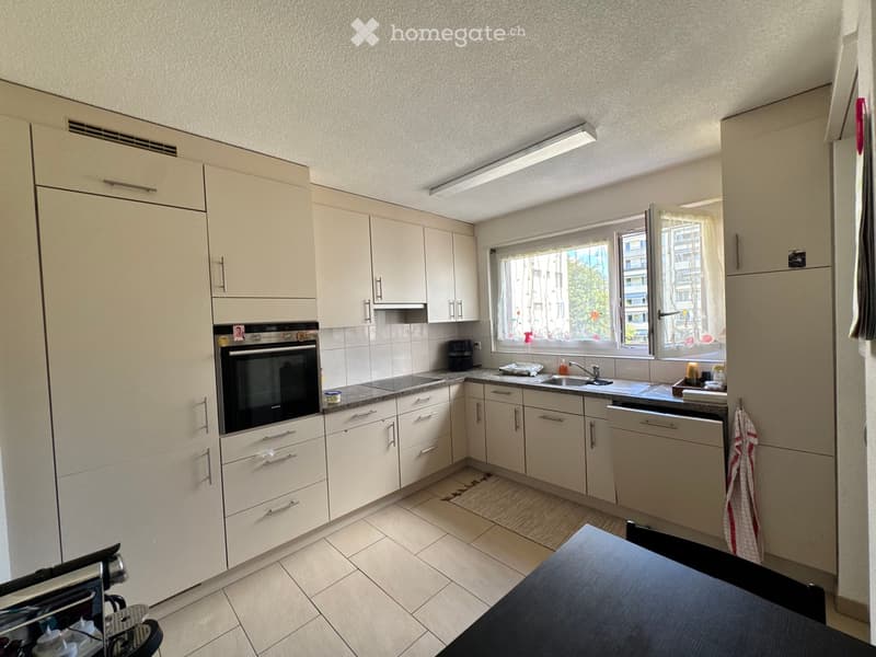 Modern kitchen with white cabinets, stainless steel appliances, granite countertop, and a window overlooking a cityscape.