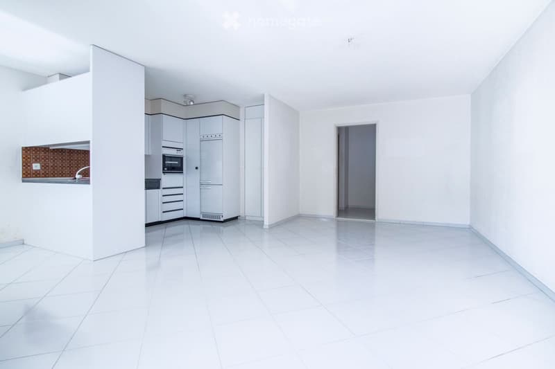 Empty kitchen with white tiled flooring, white cabinets, and stainless steel appliances including a refrigerator, microwave, and oven. The space is well-lit with a modern design and an open layout.