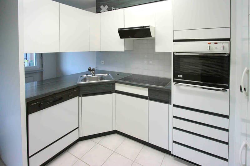 Modern kitchen with white cabinets, stainless steel appliances, and a black countertop.