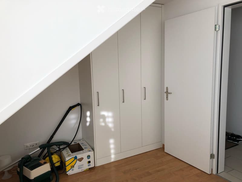 An attic space with white built-in wardrobes, wooden flooring, and a vacuum cleaner placed against the wall.