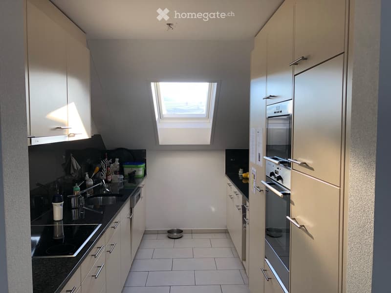 Modern kitchen with white cabinets, black countertops, and stainless steel appliances. Features a built-in oven, sink, and various small items on the counter.