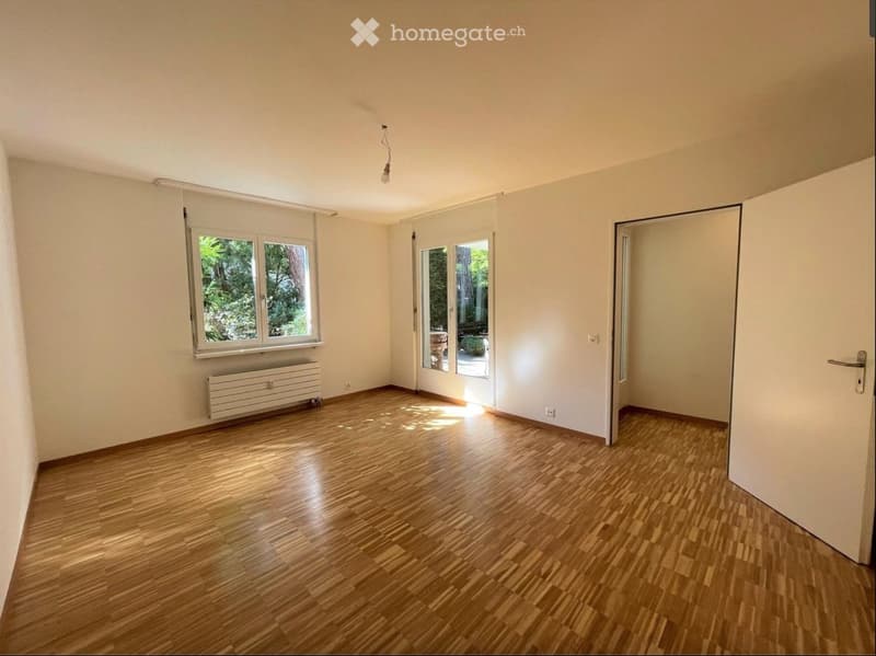 Empty room with wooden flooring, white walls, large windows, and a radiator. No furniture or equipment present.