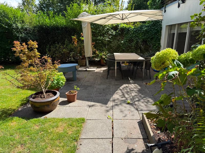 A well-maintained garden patio with a table, chairs, umbrella, and various potted plants.