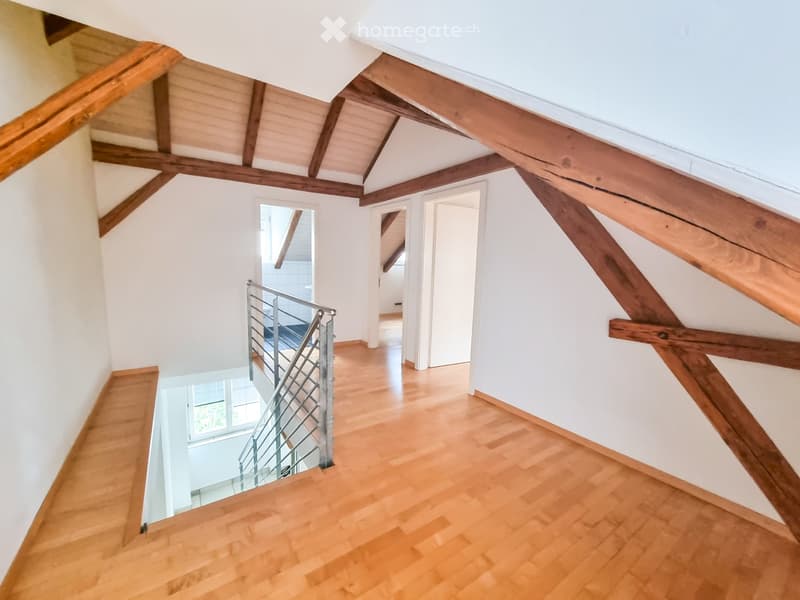 Staircase with wooden steps and a metal railing, leading to an open area with exposed wooden beams and white walls.