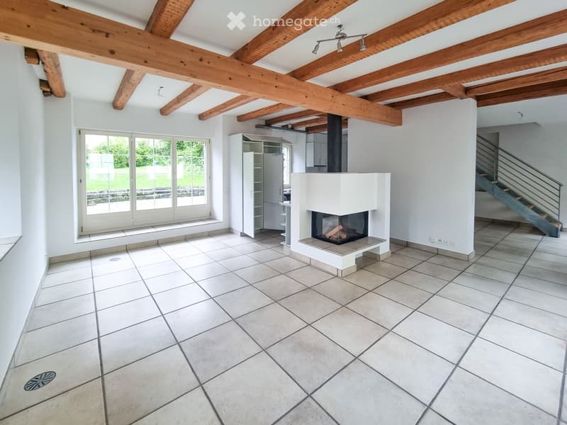 Bright living room with exposed wooden beams, large windows, fireplace, and built-in cabinet.