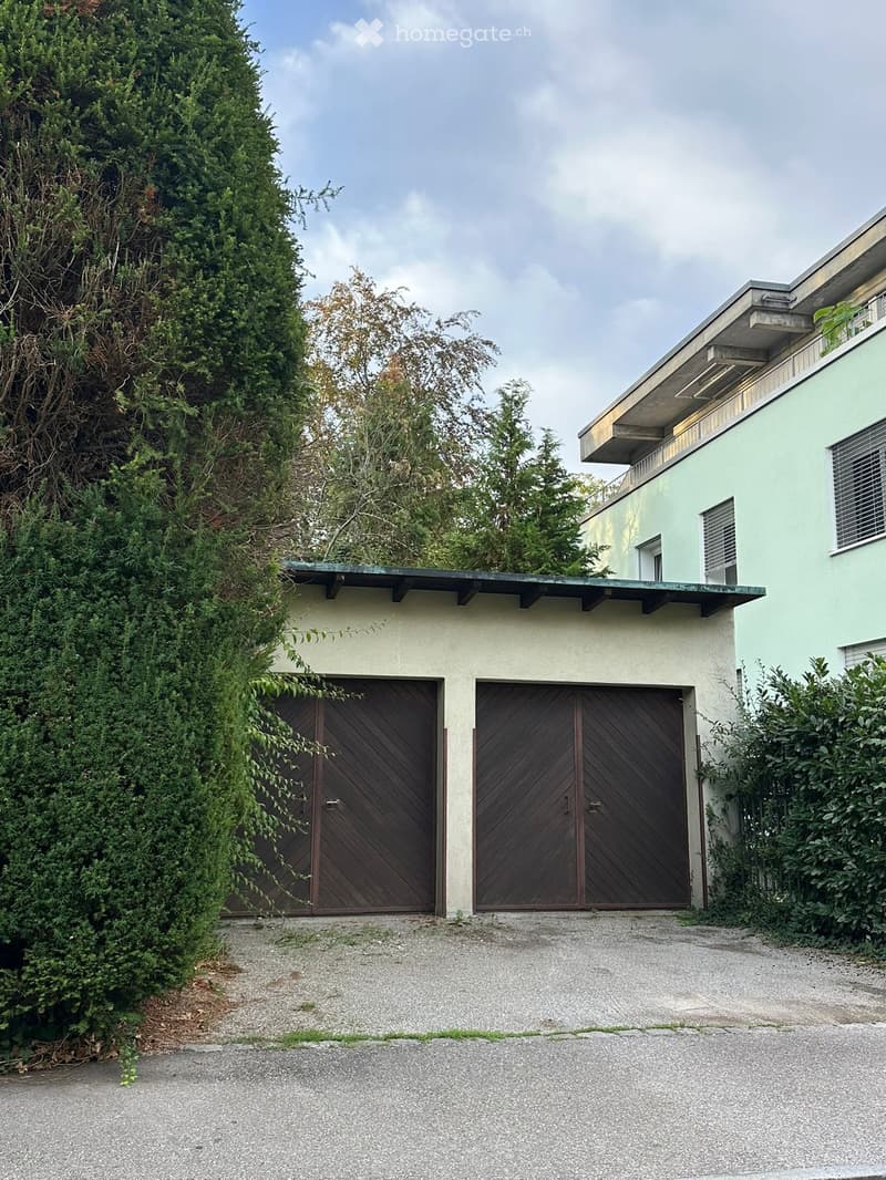 Two-story modern building with a light green facade, large wooden garage doors, and a covered entrance area.