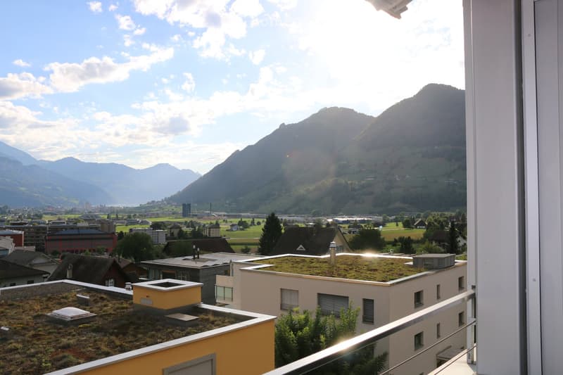 Balcony with a scenic mountain view, cityscape, and green roofs of surrounding buildings.
