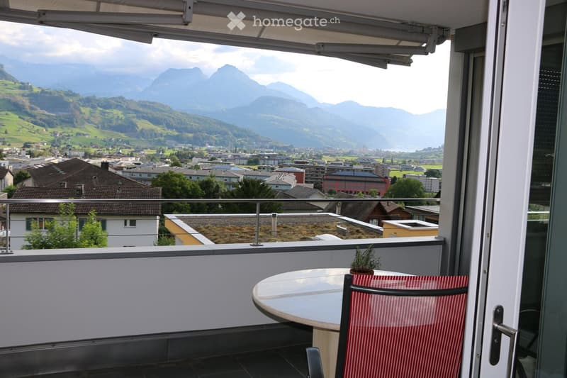 Balcony with a round table, red striped chair, small potted plant, and a scenic mountain view.