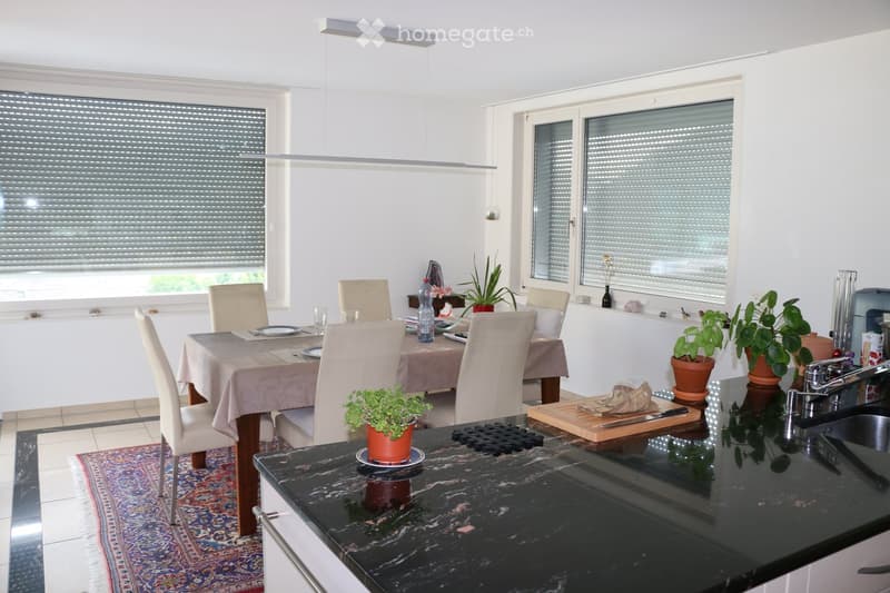 Bright, modern kitchen and dining area with white walls, large windows with blinds, marble countertop, and a dining table with chairs.