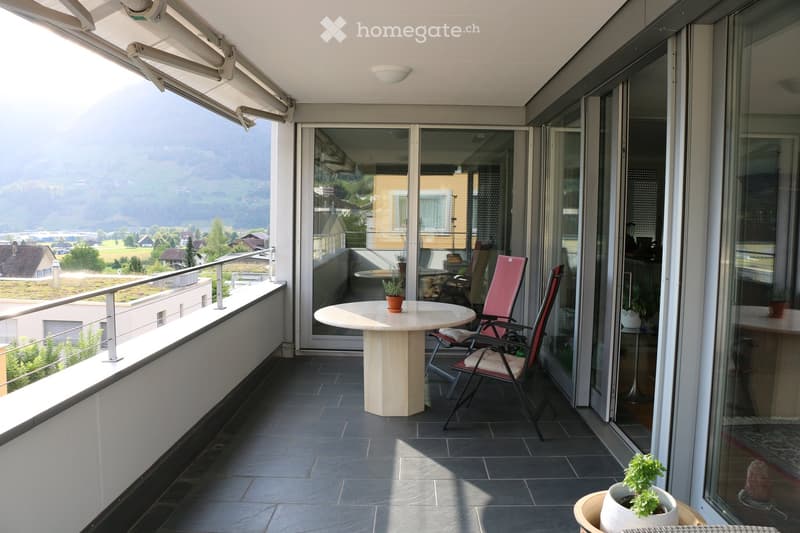 Balcony with a round table, two chairs, and potted plants, offering a scenic mountain view.
