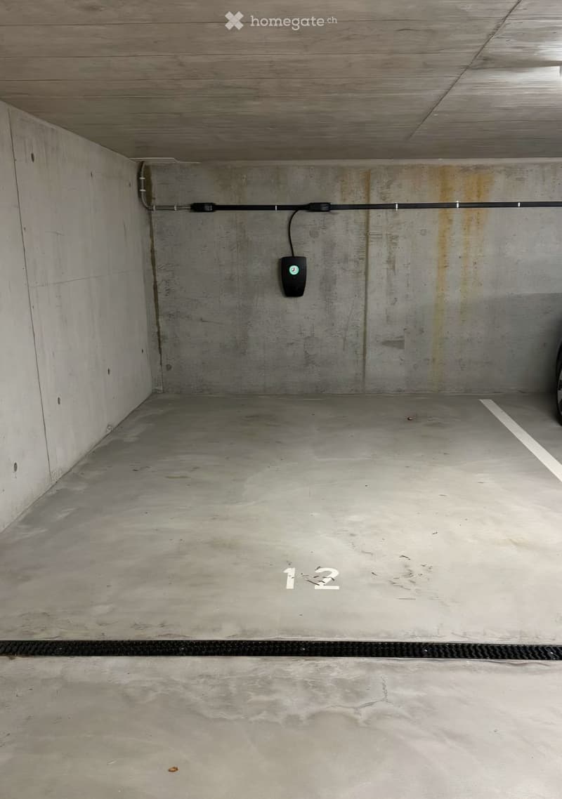Empty underground parking space with concrete walls and floor, featuring a charging station for electric vehicles.