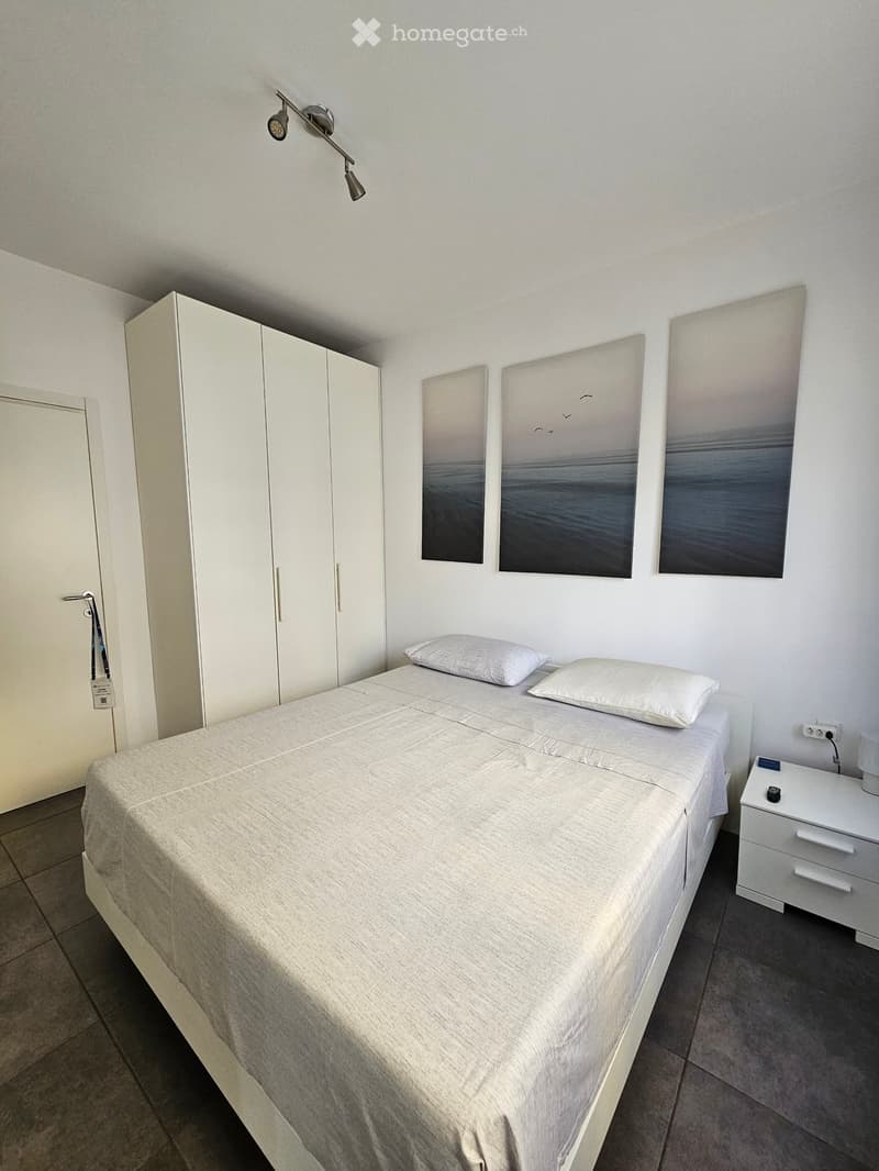 Modern bedroom with a neatly made bed, white nightstand, built-in wardrobe, and abstract artwork on the wall.