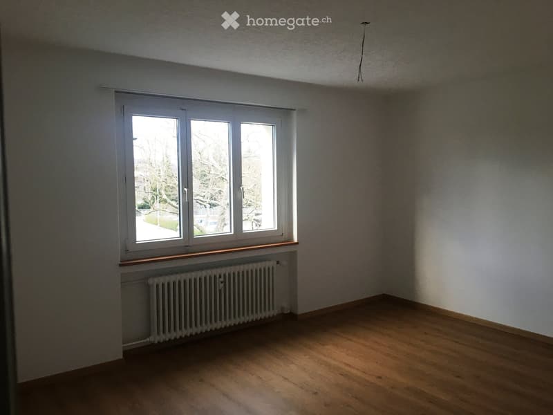Empty room with wooden flooring, white walls, large windows, radiator, and a wooden sill.