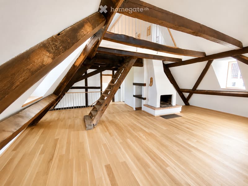 Empty attic space with wooden beams, polished wooden floor, and a white fireplace with a tiled surround.