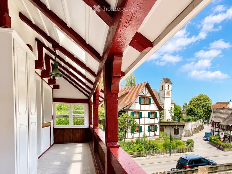 Balcony overlooking a picturesque village with traditional houses, a church tower, and a clear blue sky.