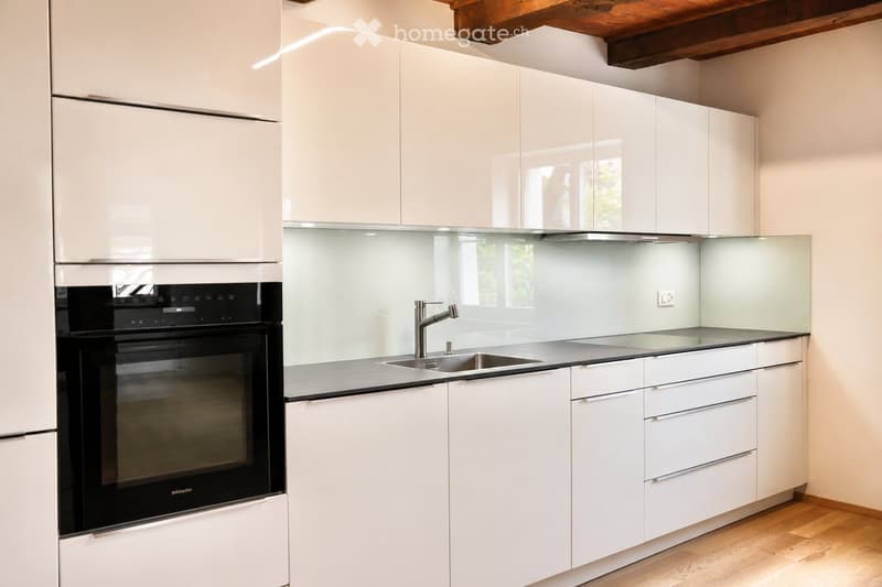 Modern kitchen with white cabinets, a stainless steel sink, a modern faucet, and a built-in oven. The countertops are sleek and the space is well-lit with natural light coming through a window.