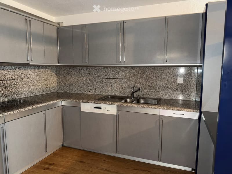 Modern kitchen with grey cabinets, granite countertops, and a stainless steel sink.