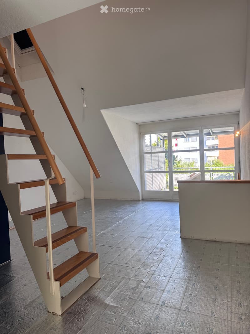 Empty room with wooden staircase, large windows, and grey tiled floor.