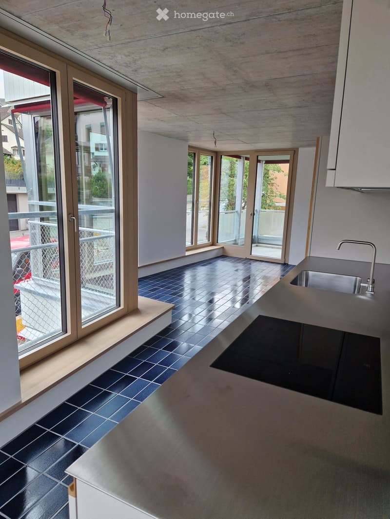 Modern kitchen with dark blue tiles, sleek countertops, and large windows leading to a balcony.