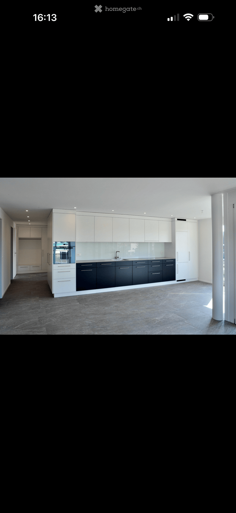 Modern kitchen with white upper cabinets, dark lower cabinets, and a central island. Features a sleek, minimalist design with a large sink and faucet.