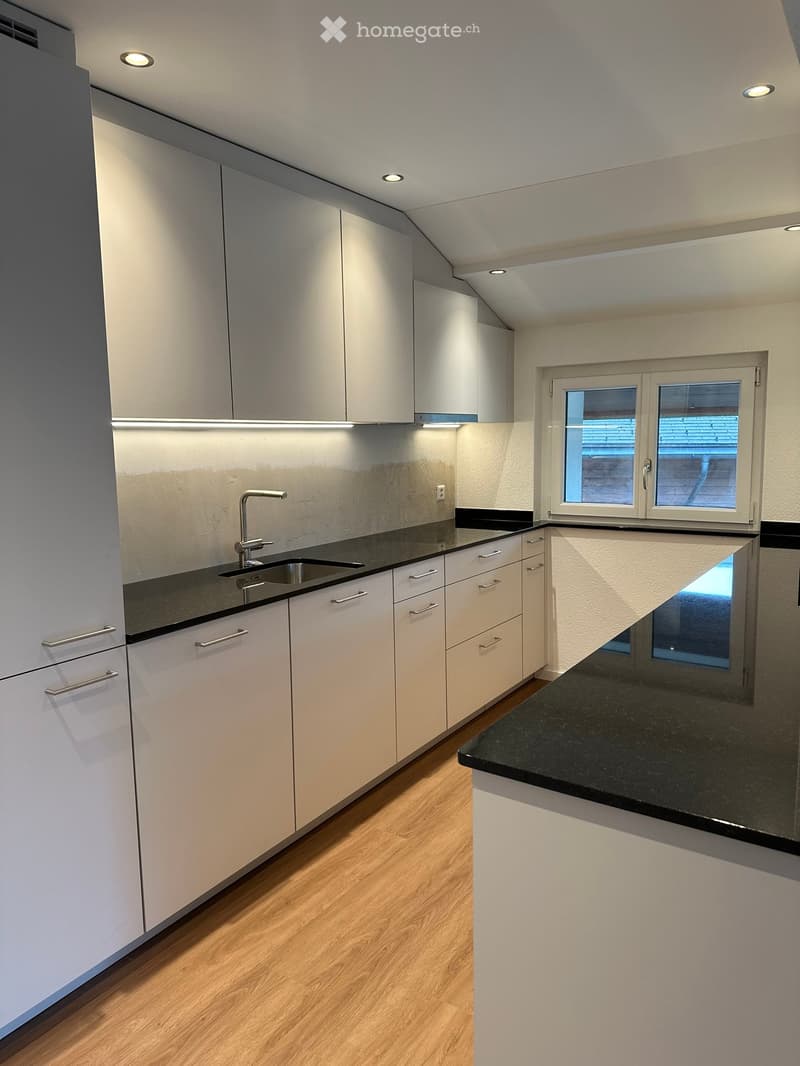 Modern kitchen with white cabinets, black countertops, and a stainless steel sink.