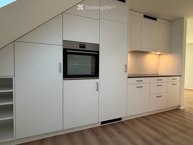 Modern kitchen with white cabinets, built-in oven, and wooden flooring.