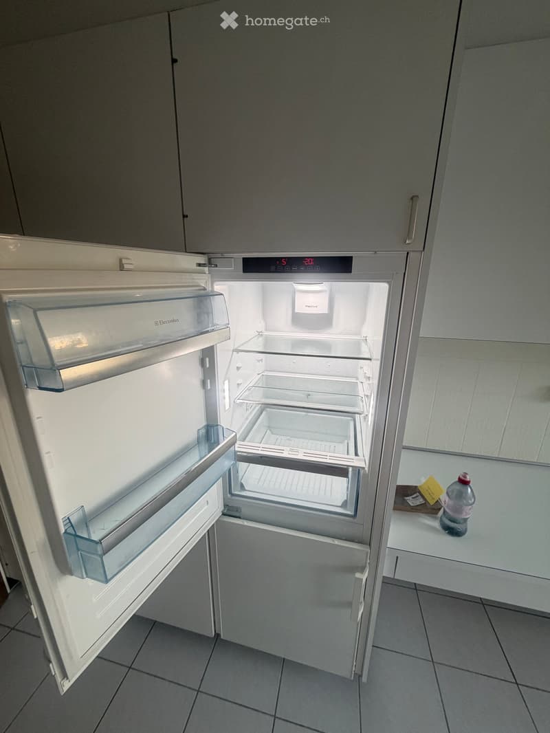 Open refrigerator with shelves and drawers, placed next to a countertop with a bottle on it.